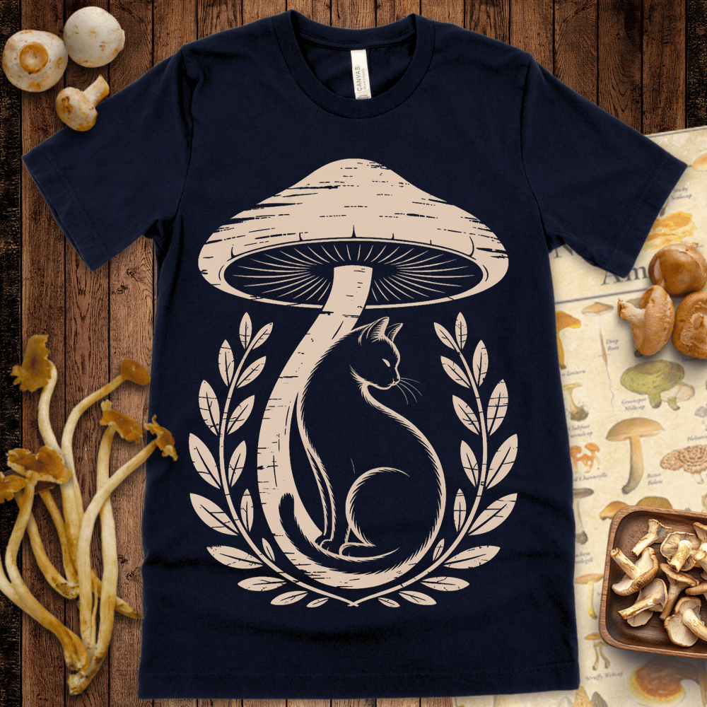 Illustration of a black cat sitting beneath a large vintage mushroom, framed by botanical laurels on a t-shirt design