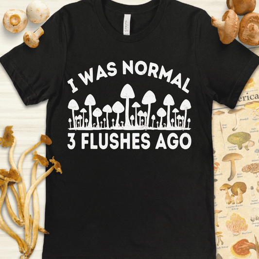 Black T-shirt design with white mushrooms and the phrase "I Was Normal 3 Flushes Ago," referencing multiple mushroom harvests.