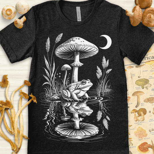Surreal black and white drawing of a frog sitting beneath mushrooms at night, reflected in a pond under a crescent moon.