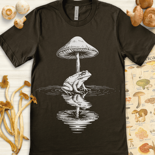 Black-and-white surreal illustration of a frog under a mushroom, reflected in rippling water with abstract dark shapes above.